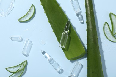 Flat lay composition with skincare ampoules and aloe leaves on light blue background