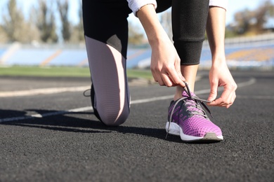 Image of Sporty woman tying shoelaces at stadium on sunny morning, closeup