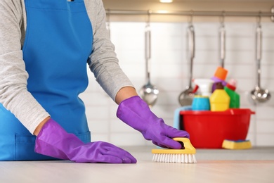 Woman cleaning table with brush in kitchen, closeup