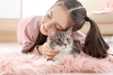 Photo of Cute little girl with cat lying on floor at home