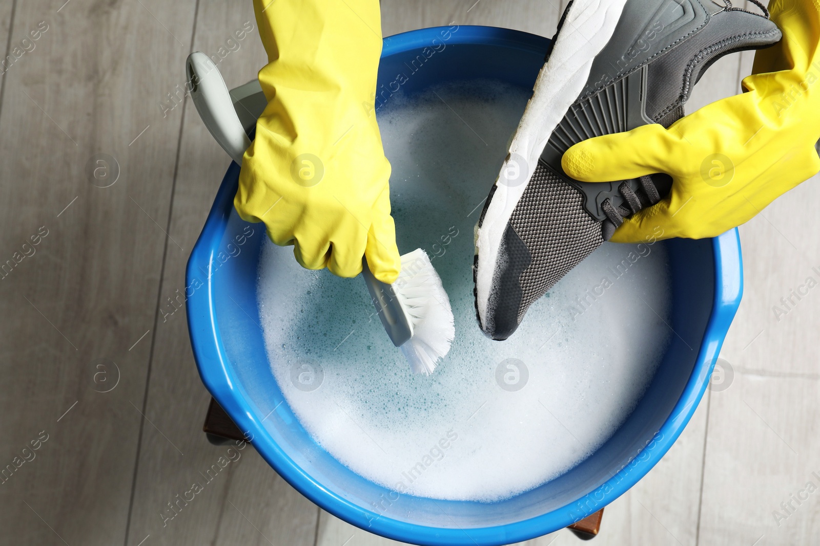 Photo of Woman with gloves and brush cleaning stylish sneakers in wash basin, top view