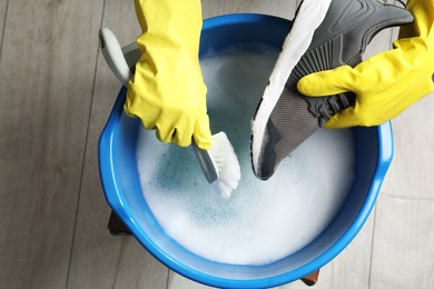 Photo of Woman with gloves and brush cleaning stylish sneakers in wash basin, top view