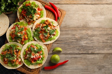 Delicious tacos with vegetables, meat and lime on wooden table, flat lay. Space for text