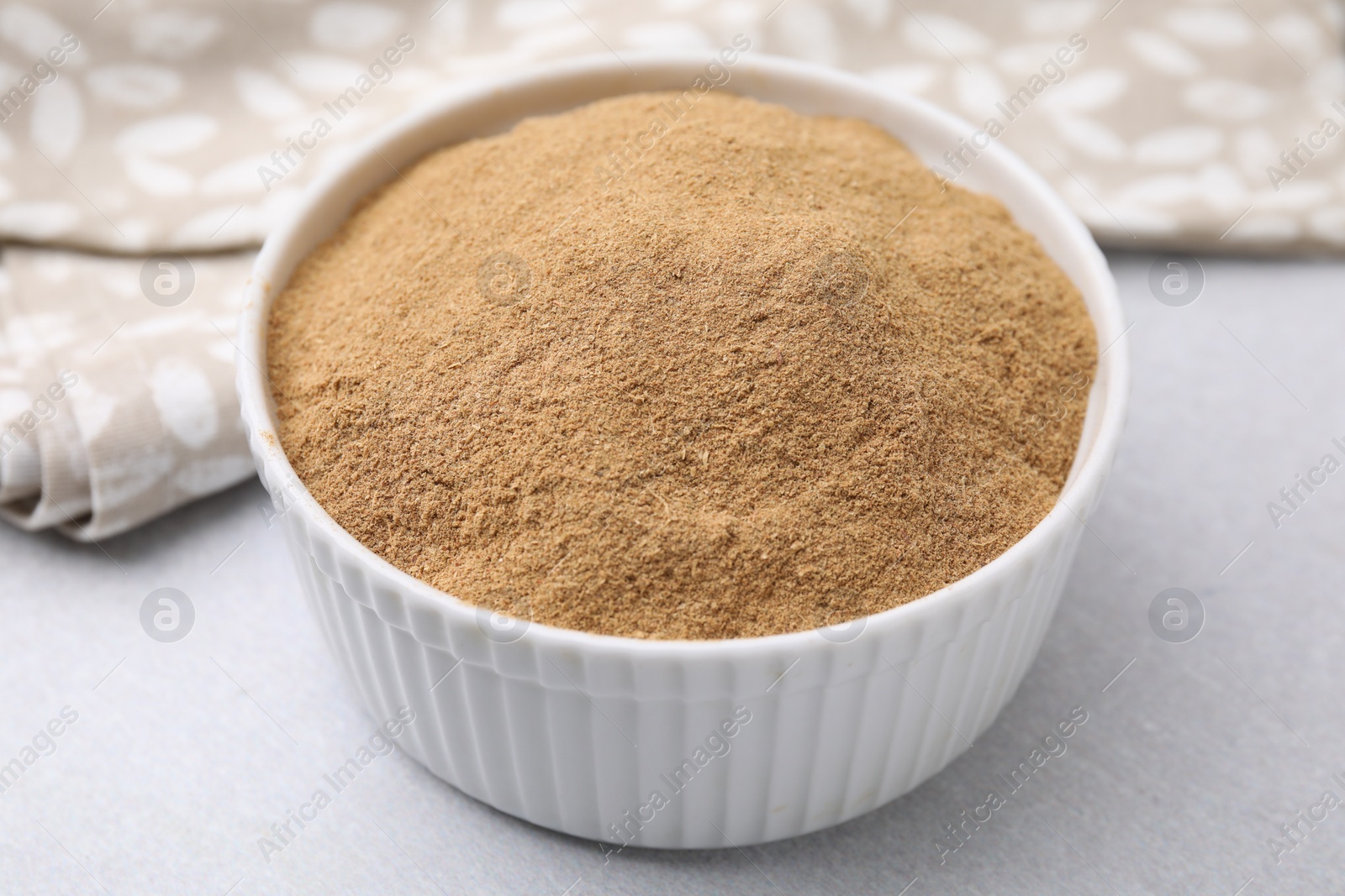 Photo of Dietary fiber. Psyllium husk powder in bowl on light grey table, closeup