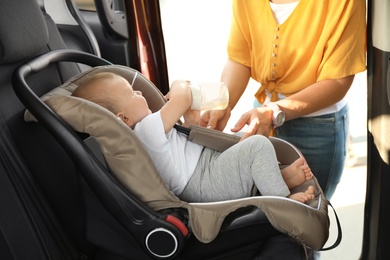 Photo of Mother fastening baby to child safety seat inside of car