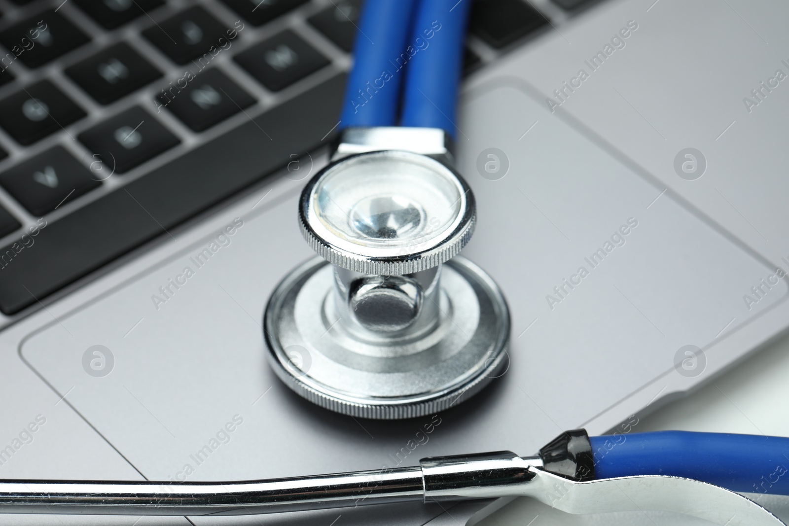 Photo of Stethoscope and modern laptop on grey table, closeup