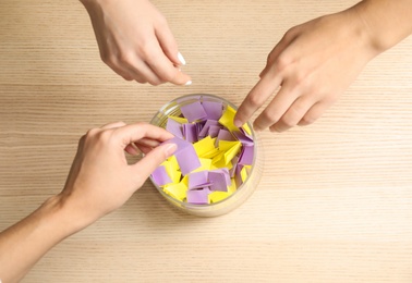 Photo of Women playing lottery, focus on hands and glass vase with paper pieces