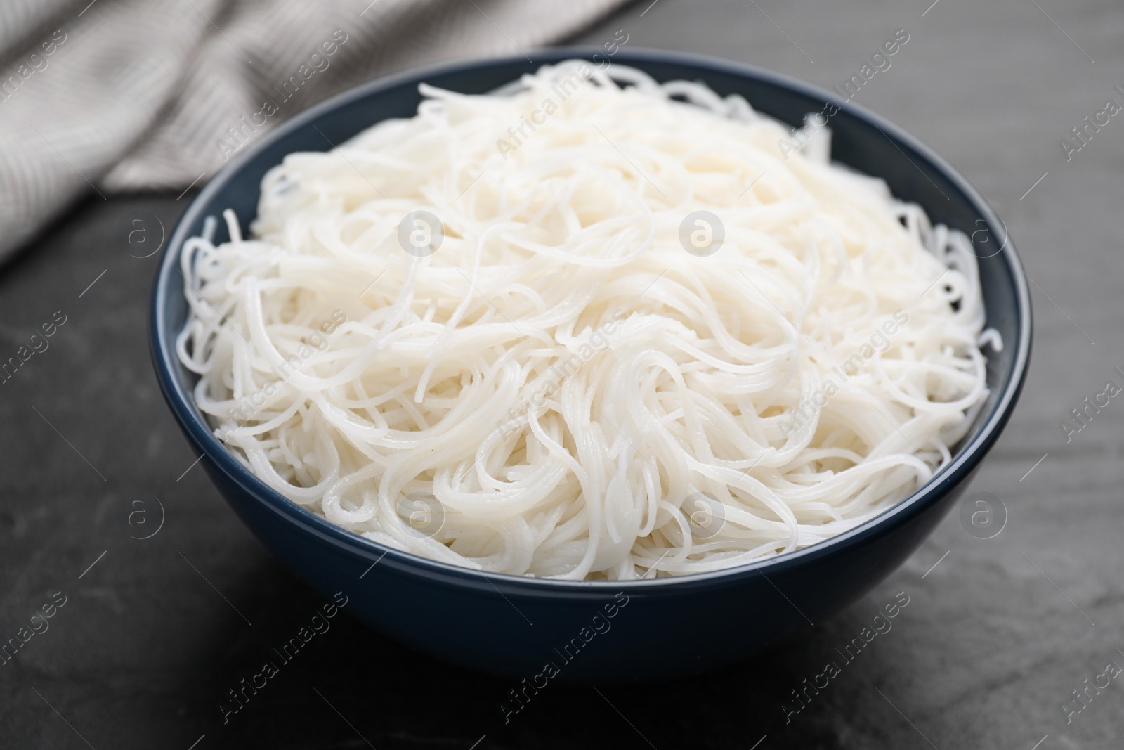 Photo of Bowl with cooked rice noodles on black table, closeup