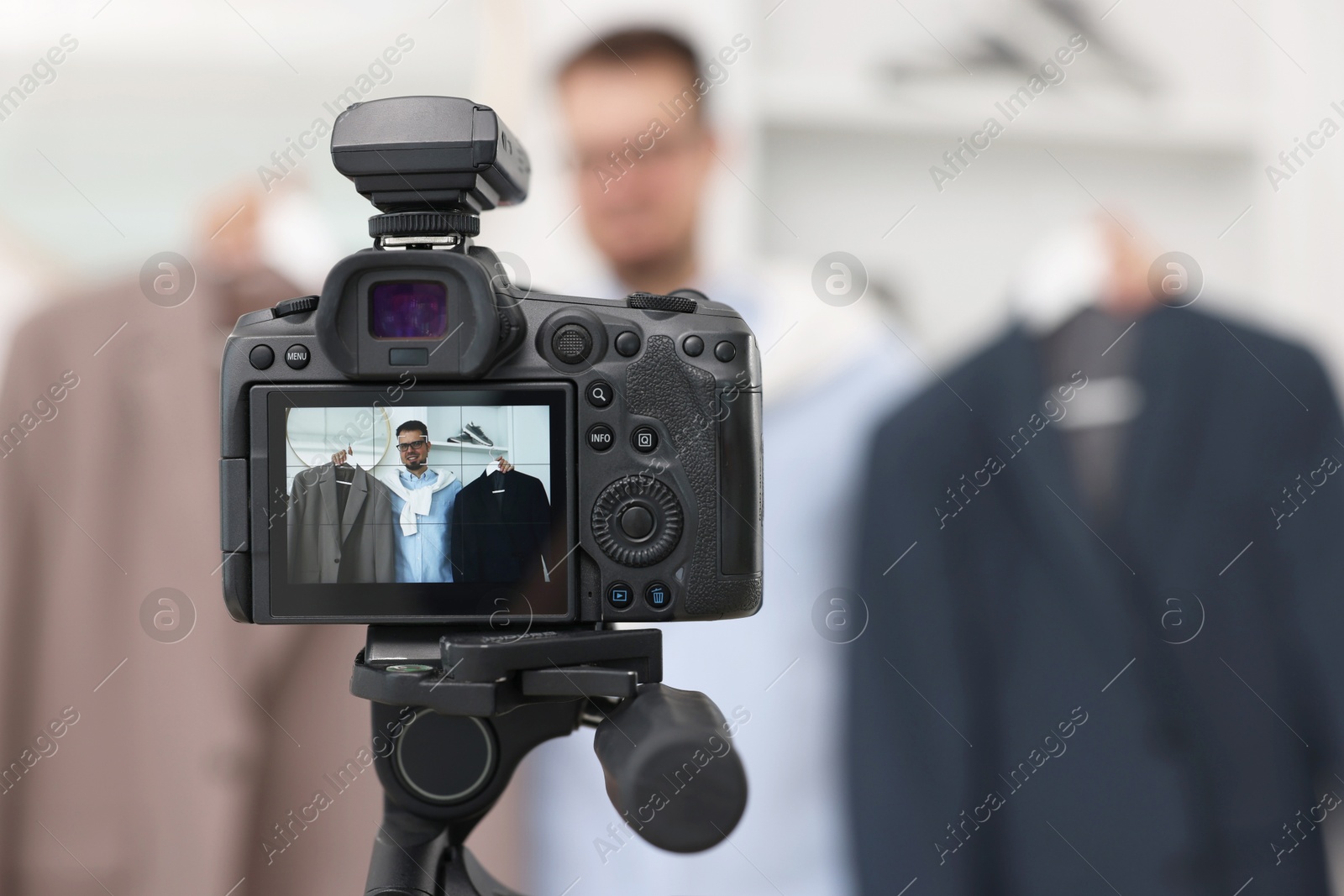 Photo of Fashion blogger showing clothes while recording video at home, focus on camera