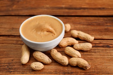 Photo of Delicious nut butter in bowl and peanuts on wooden table, closeup