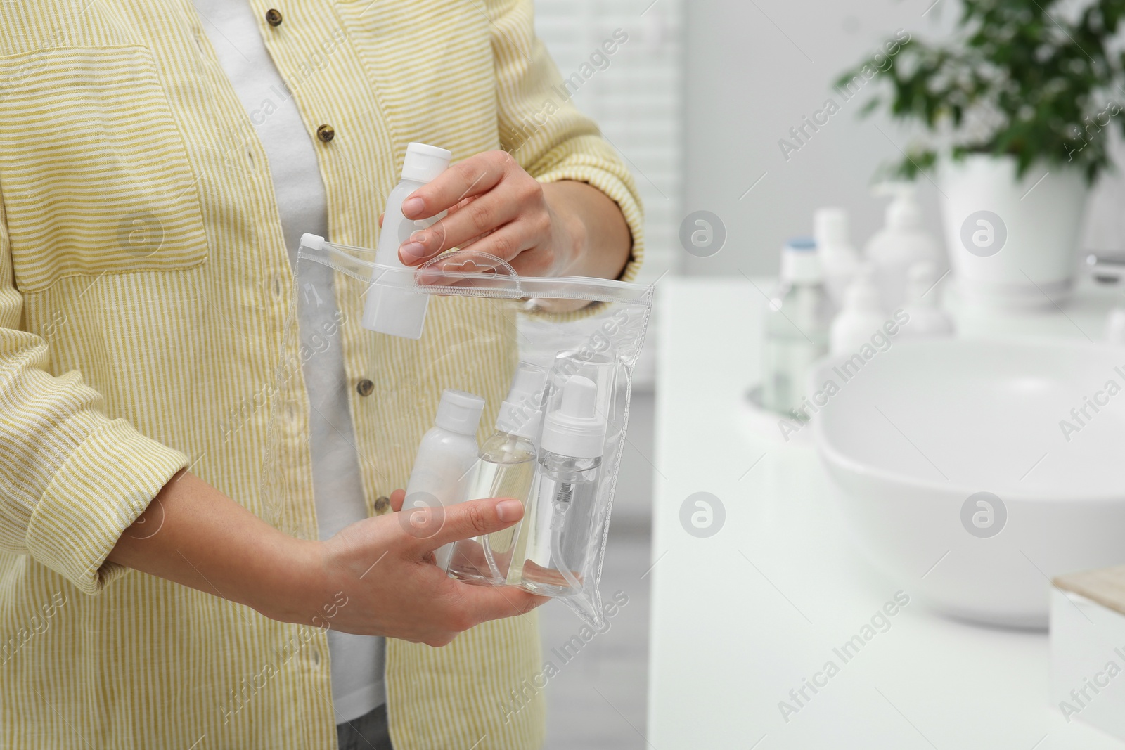 Photo of Woman packing cosmetic travel kit in bathroom, closeup and space for text. Bath accessories