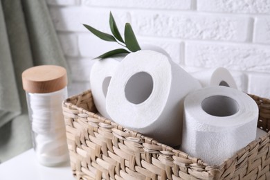 Photo of Toilet paper rolls in wicker basket, floral decor and cotton pads on table
