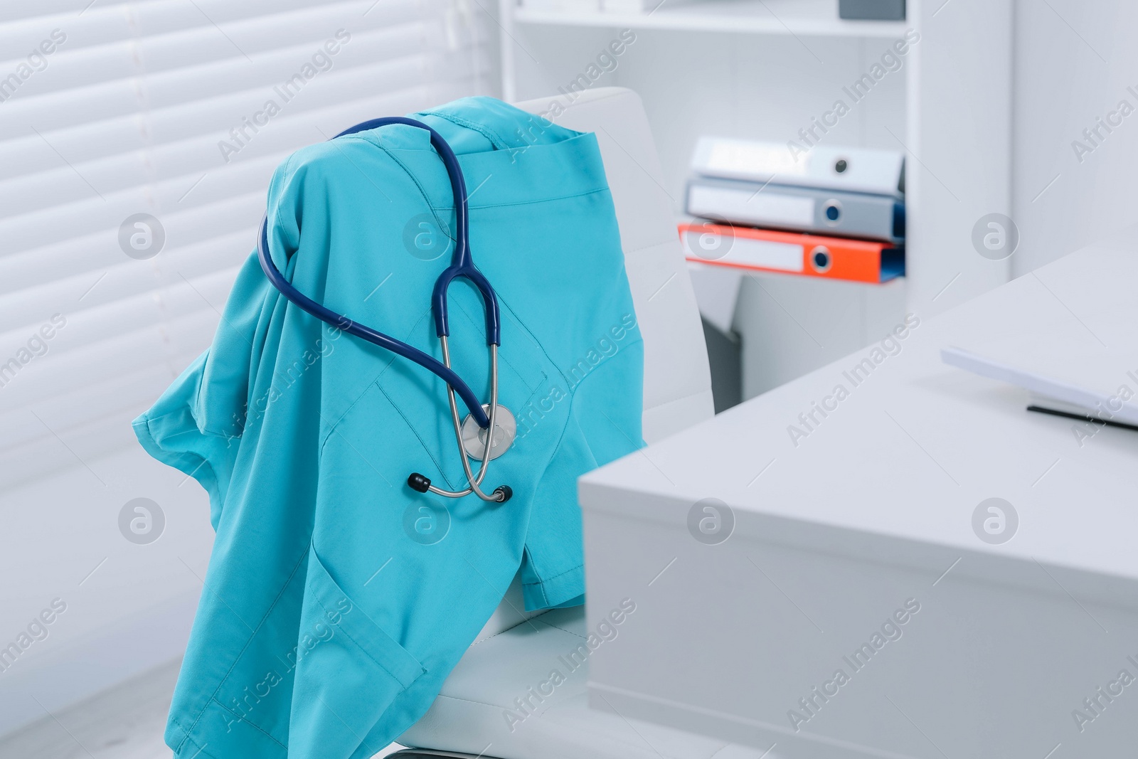 Photo of Turquoise medical uniform and stethoscope hanging on chair in clinic