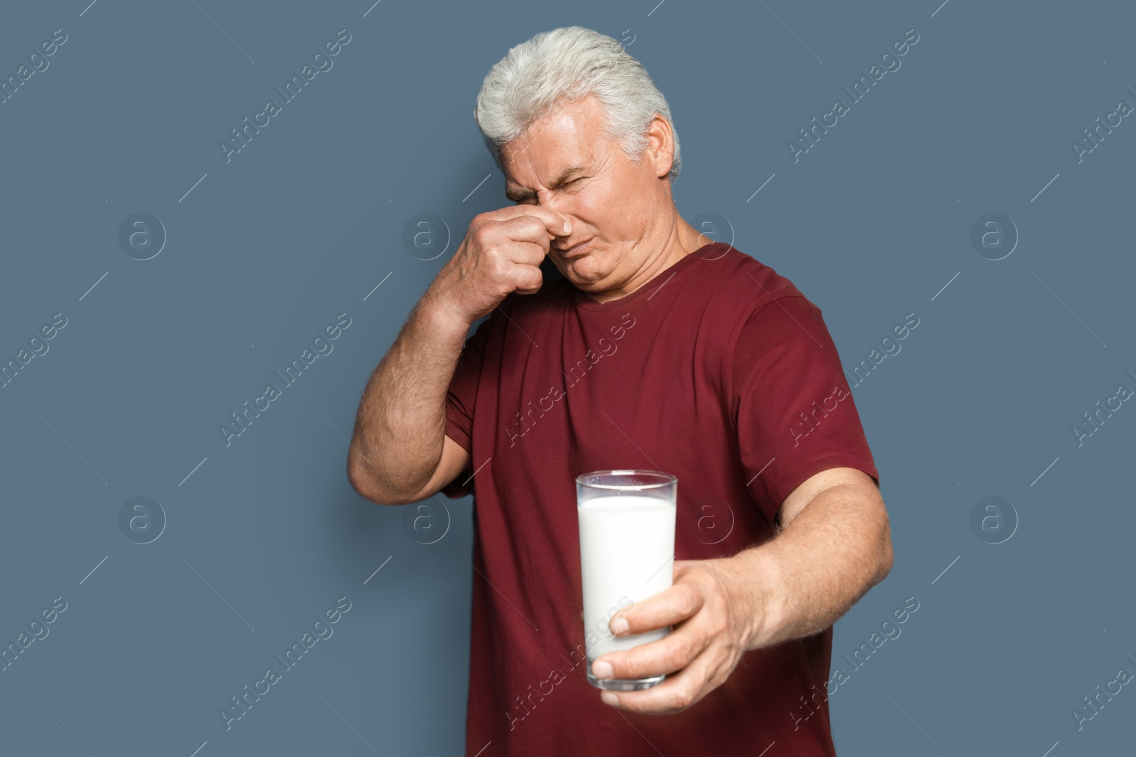 Photo of Mature man with dairy allergy holding glass of milk on color background