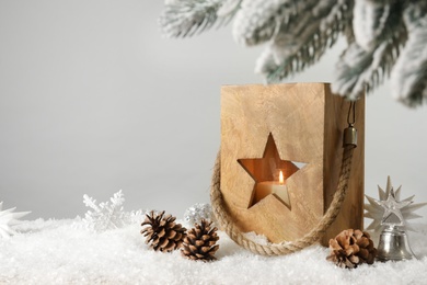 Composition with wooden Christmas lantern on snow against light grey background, space for text