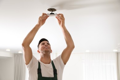 Electrician in uniform repairing lamp on ceiling indoors. Space for text