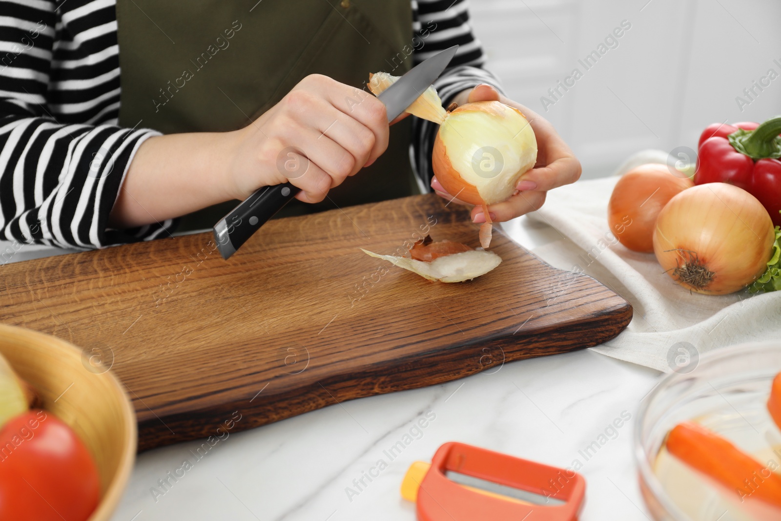 Photo of Woman peeling fresh onion with knife at white marble table indoors, closeup