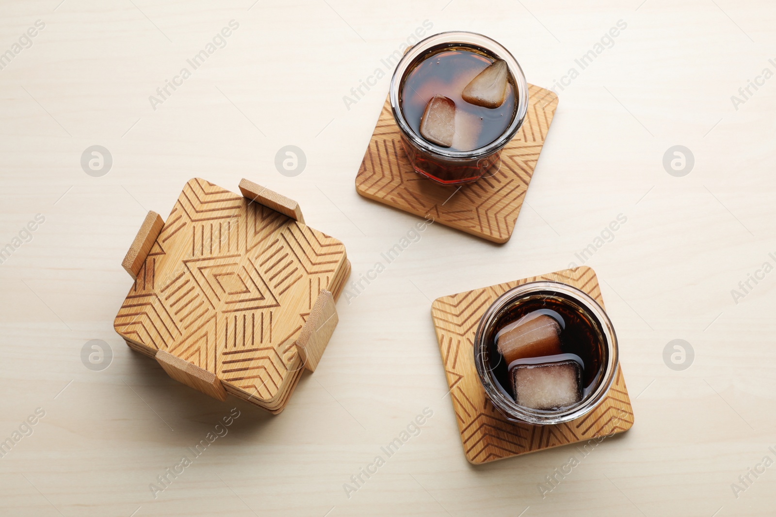 Photo of Glasses of cold drink with ice cubes and stylish wooden cup coasters on table, flat lay