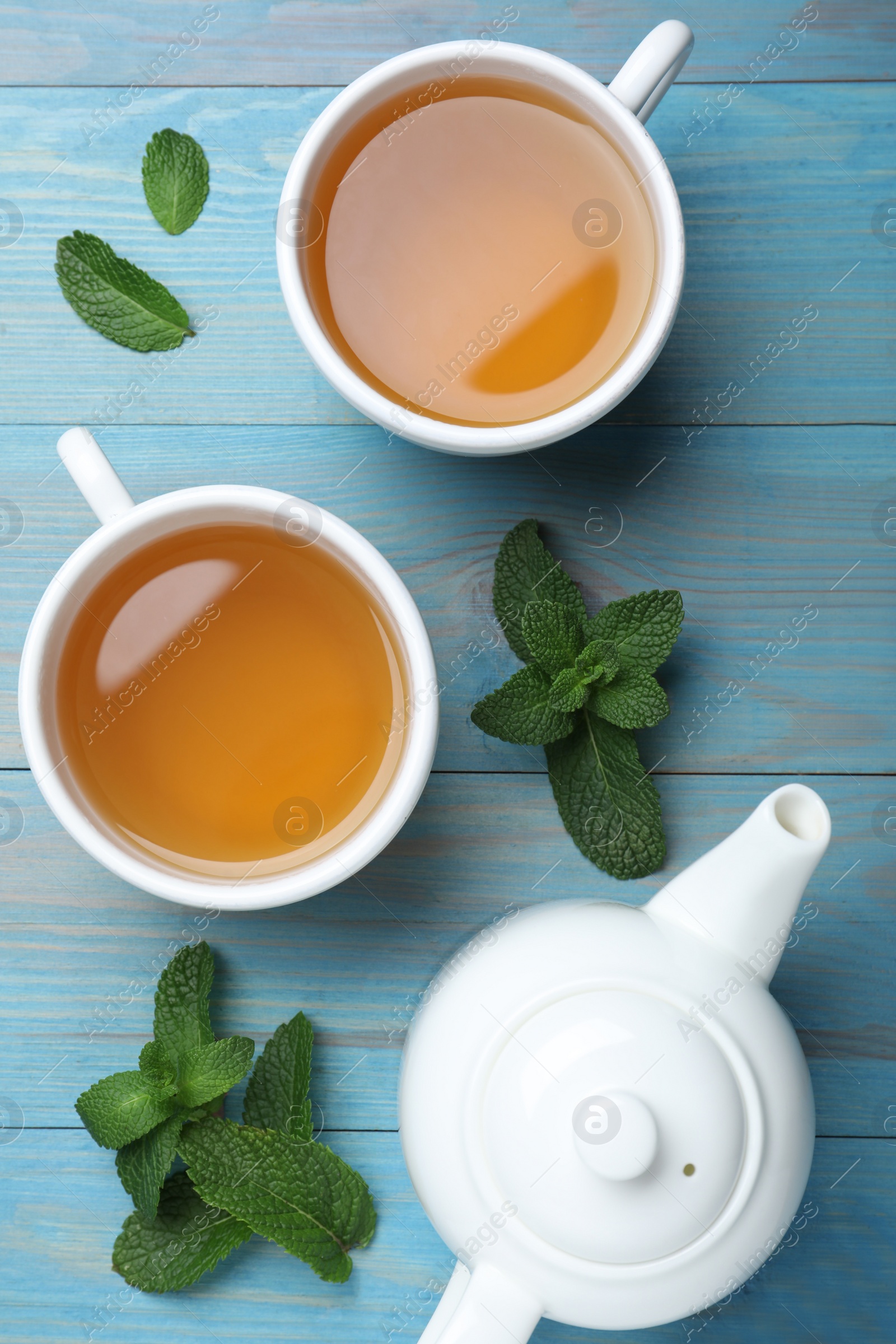 Photo of Hot aromatic mint tea on light blue wooden table, flat lay