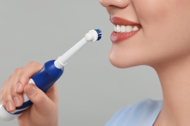 Woman brushing her teeth with electric toothbrush on light grey background, closeup