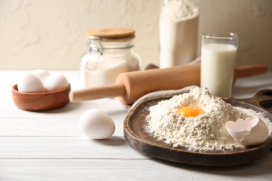 Making dough. Pile of flour with yolk, rolling pin and eggs on white wooden table, closeup