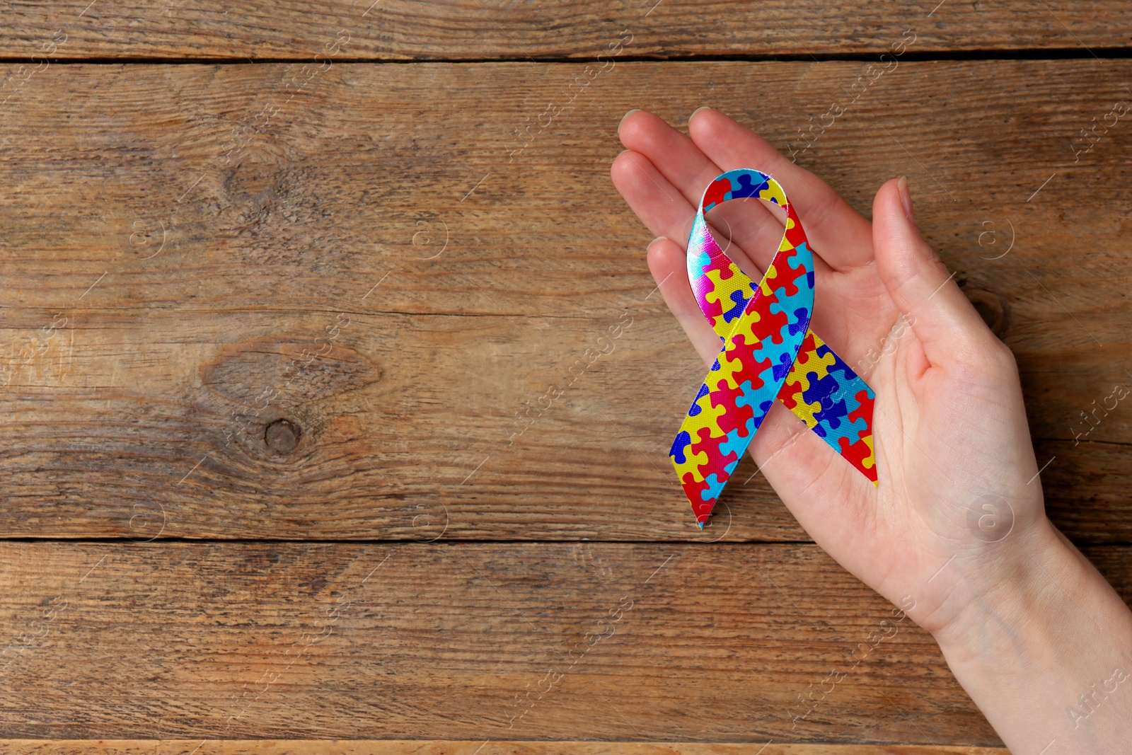 Image of World Autism Awareness Day. Woman with colorful puzzle ribbon on wooden background, top view with space for text