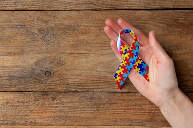 Image of World Autism Awareness Day. Woman with colorful puzzle ribbon on wooden background, top view with space for text