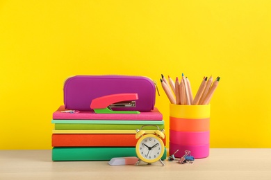 Different school stationery and alarm clock on table against yellow background. Back to school