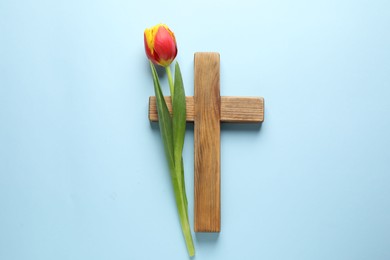 Easter - celebration of Jesus resurrection. Wooden cross and tulip on light blue background, top view
