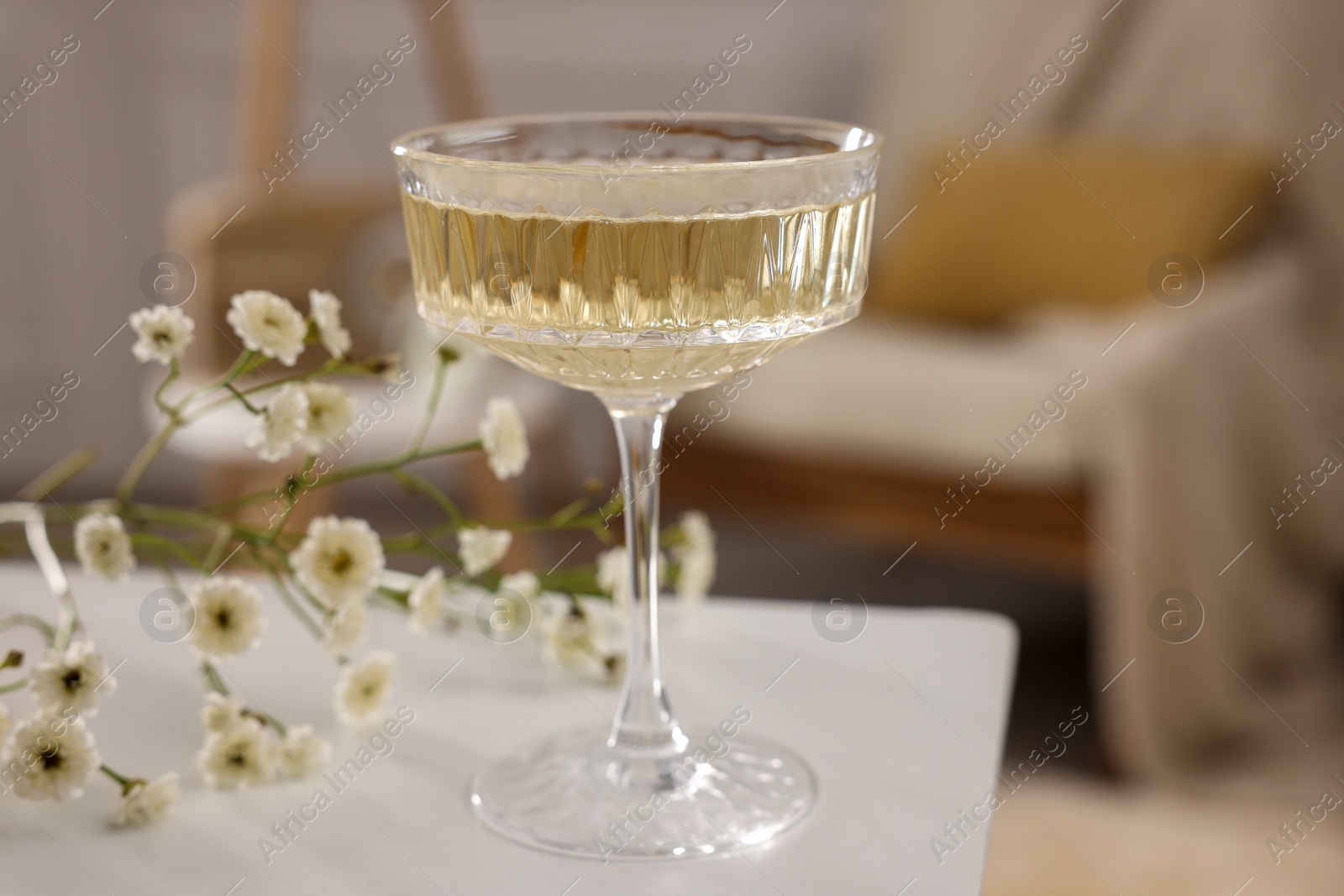 Photo of Glass of alcohol drink and flowers on table in room. Relax at home