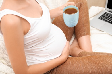 Pregnant woman with laptop drinking tea at home, closeup