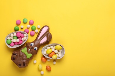 Chocolate Easter bunny, halves of egg and candies on yellow background, flat lay. Space for text