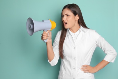 Young female doctor using megaphone on color background