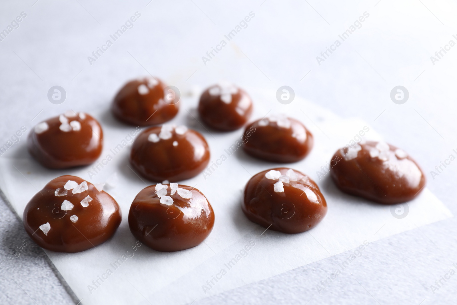 Photo of Tasty caramel candies and salt on light grey table, closeup