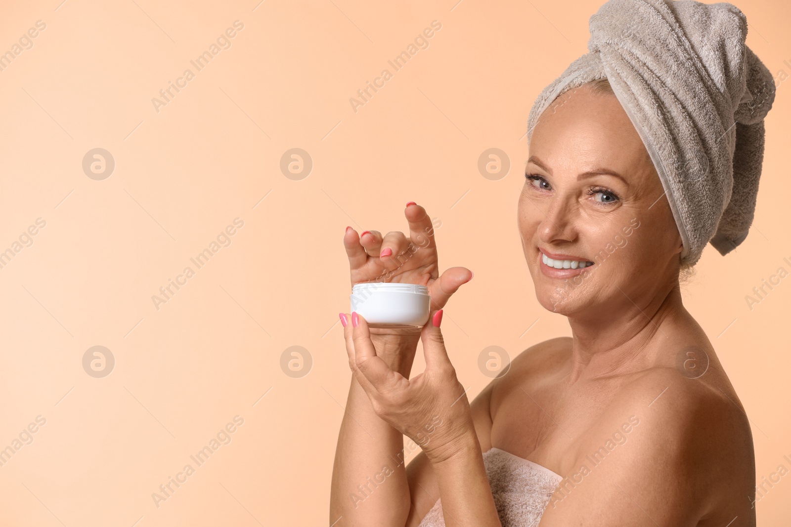 Photo of Portrait of beautiful mature woman with perfect skin holding jar of cream on beige background. Space for text