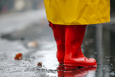 Woman in rubber boots walking outdoors on rainy day, closeup. Space for text