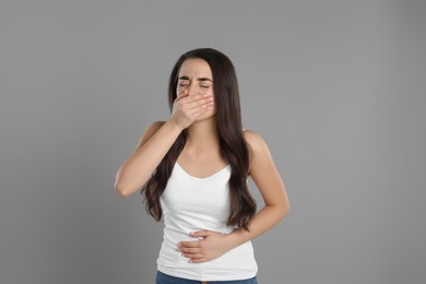 Young woman suffering from nausea on grey background. Food poisoning