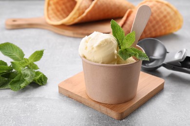 Delicious vanilla ice cream with mint in paper cup on light grey table, closeup