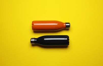 Photo of Modern thermo bottles on yellow background, flat lay