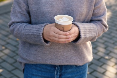 Photo of Woman holding takeaway cardboard cup on city street, closeup. Coffee to go