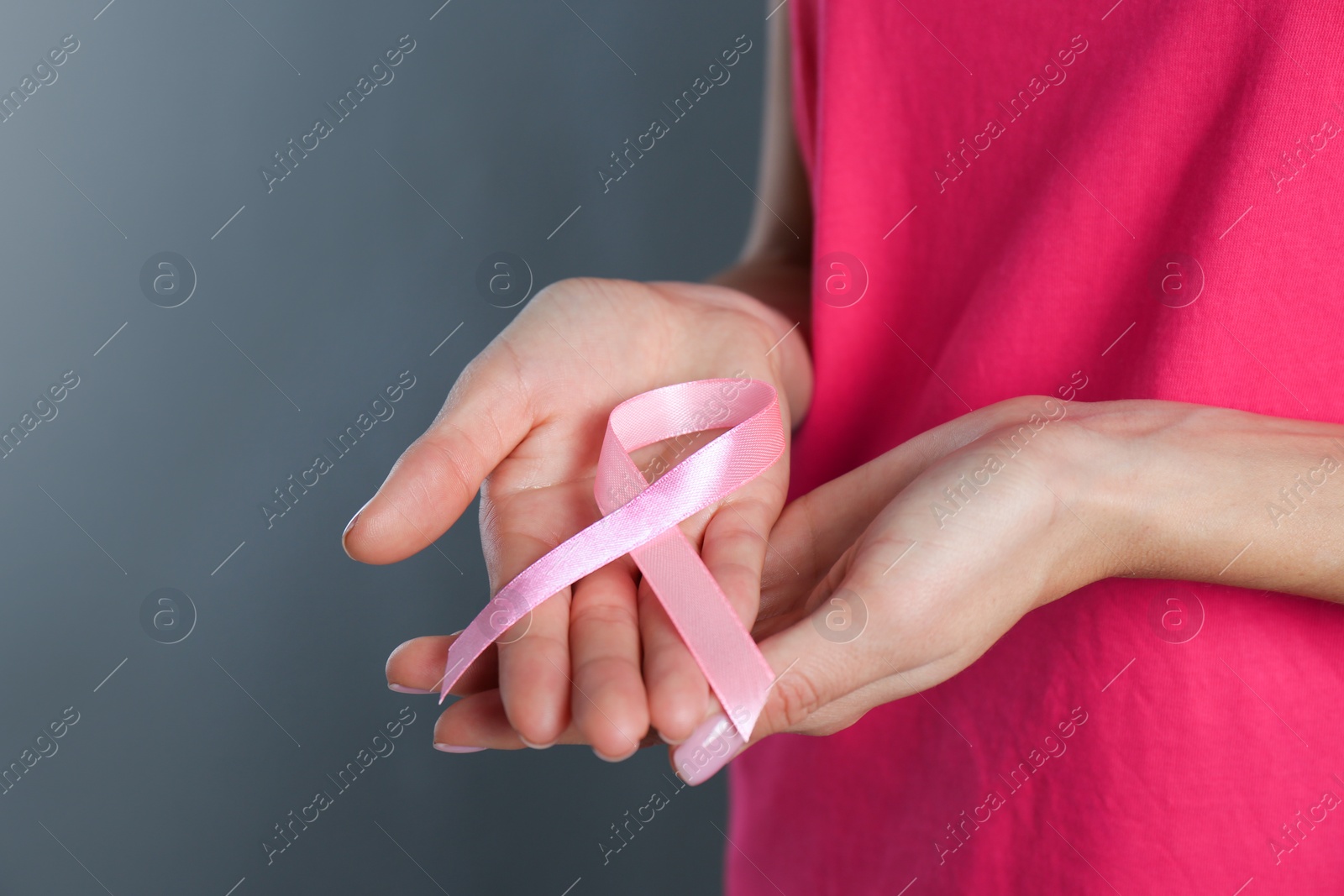 Photo of Woman holding pink ribbon on grey background, closeup with space for text. Breast cancer awareness