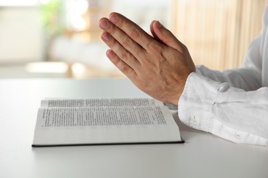 Photo of Man with Bible praying at white table indoors, closeup