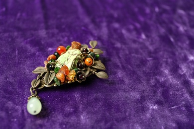 Photo of Beautiful brooch with gemstones on violet fabric. Space for text