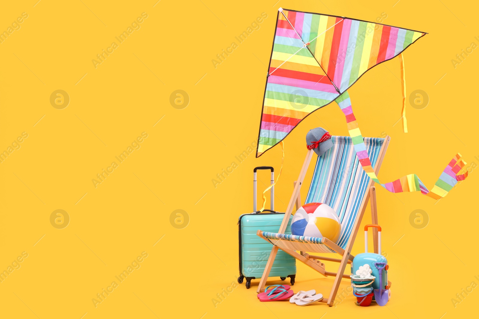 Photo of Deck chair, kite, suitcases and beach accessories against orange background, space for text. Summer vacation