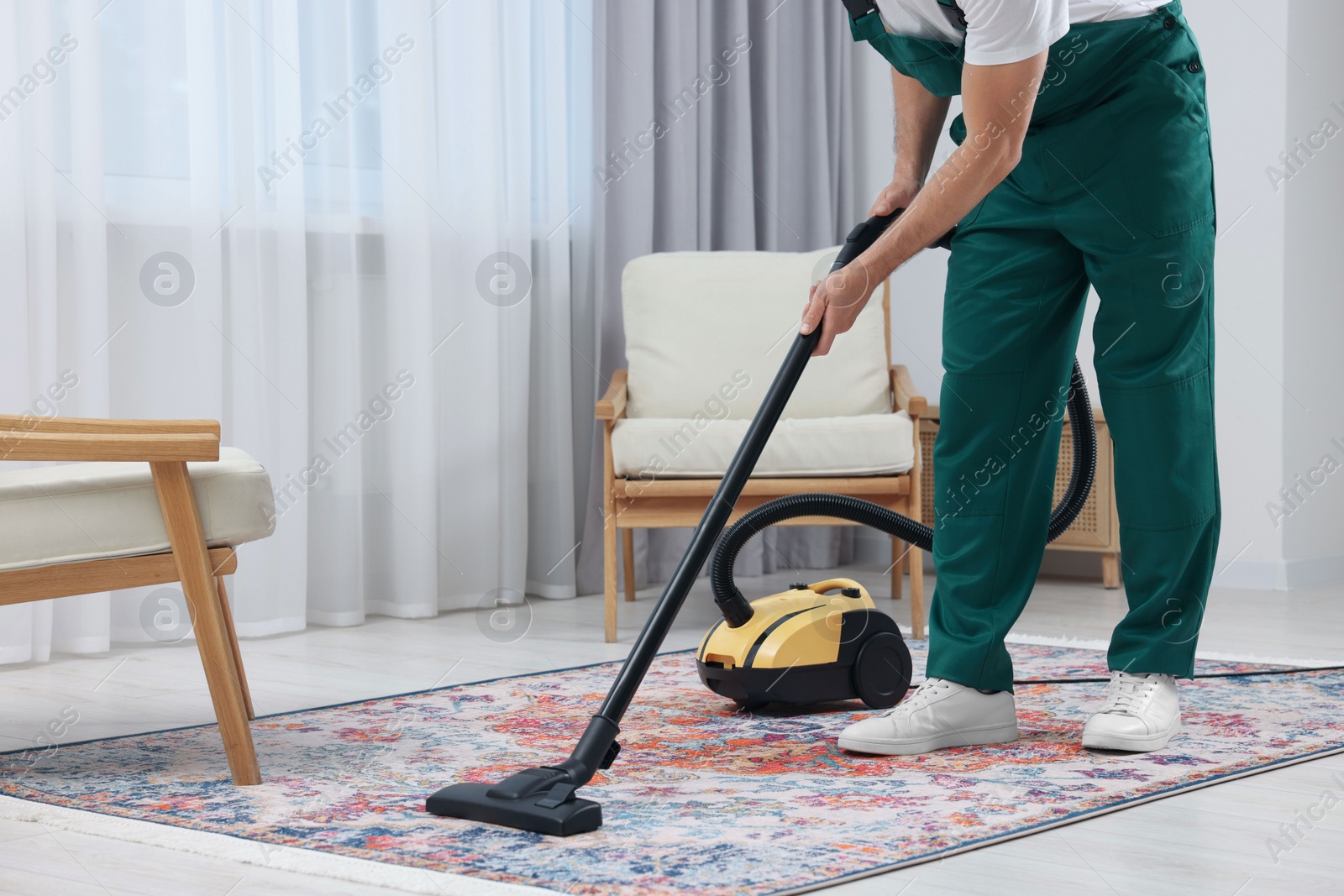 Photo of Dry cleaner's employee hoovering carpet with vacuum cleaner in room, closeup