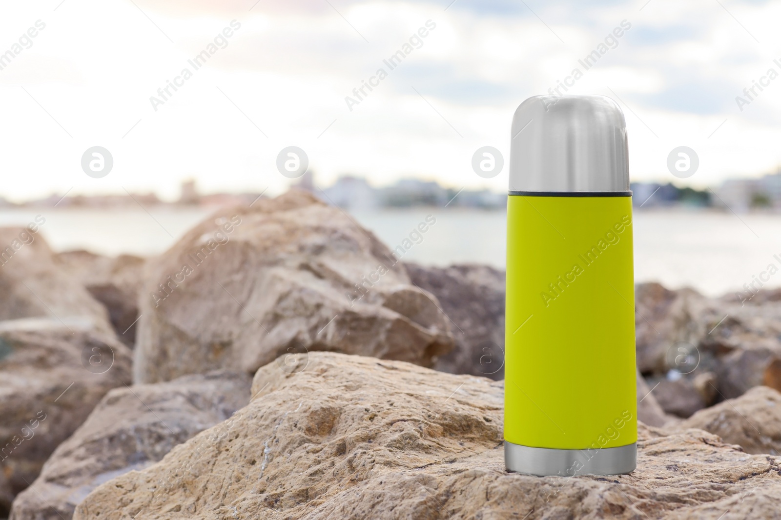 Photo of Metallic thermos with hot drink on stone near sea, space for text