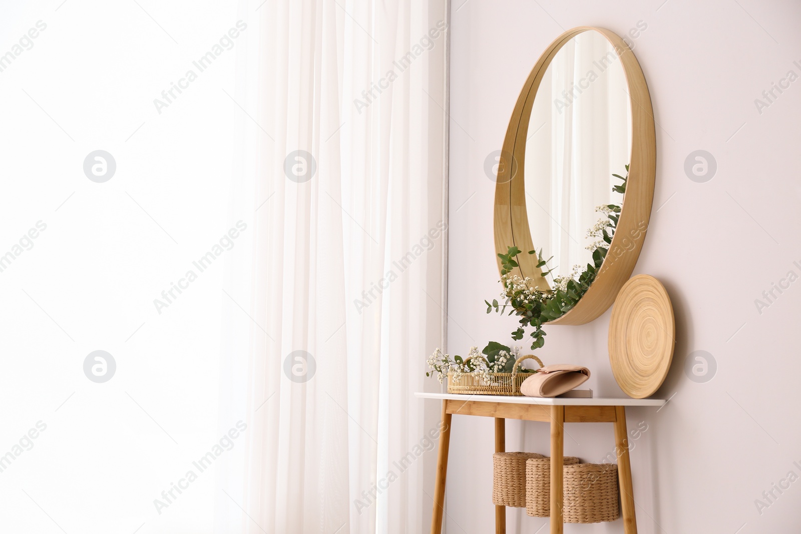 Photo of Round mirror and table with accessories near white wall. Modern interior design