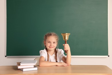 Photo of Pupil with school bell sitting at desk near chalkboard in classroom, space for text