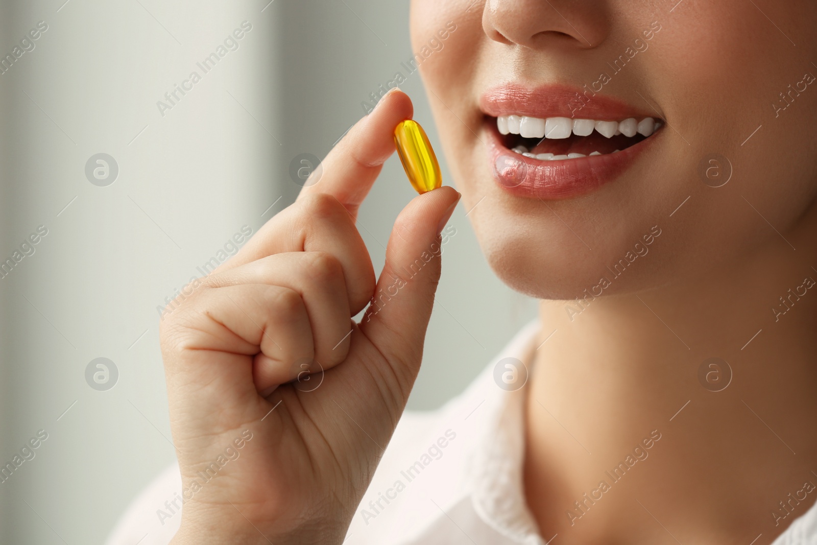 Photo of Young woman taking dietary supplement pill on blurred background, closeup