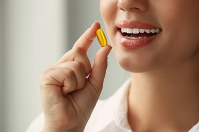 Photo of Young woman taking dietary supplement pill on blurred background, closeup
